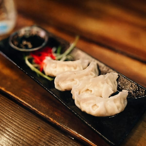 Three Oki Shōten gyoza dumplings on a black plate with soy sauce, red ginger, and green onions.