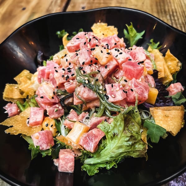 Oki Shōten's poke bowl with tuna, seaweed, mango, and sesame seeds in a black bowl.