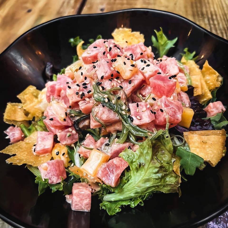 Oki Shōten's poke bowl with tuna, seaweed, mango, and sesame seeds in a black bowl.