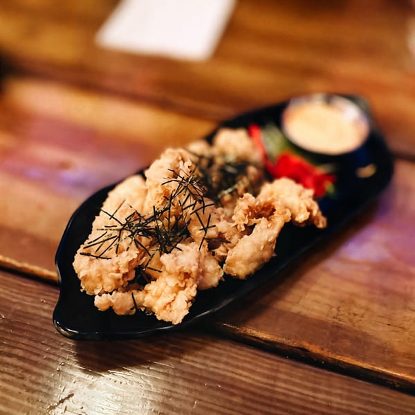 Crispy fried calamari with nori strips, red garnish, and dipping sauce on a black plate at Oki Shōten.